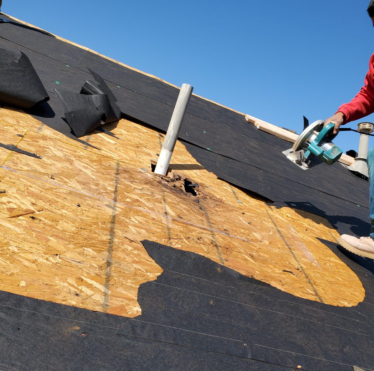 Rotted roof decking being cut out around a vent pipe during a roof repair